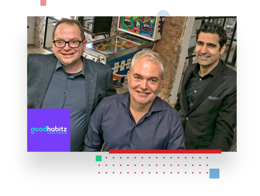 picture of three GoodHabitz employees smiling at the camera from their office, with in the background a pinball machine