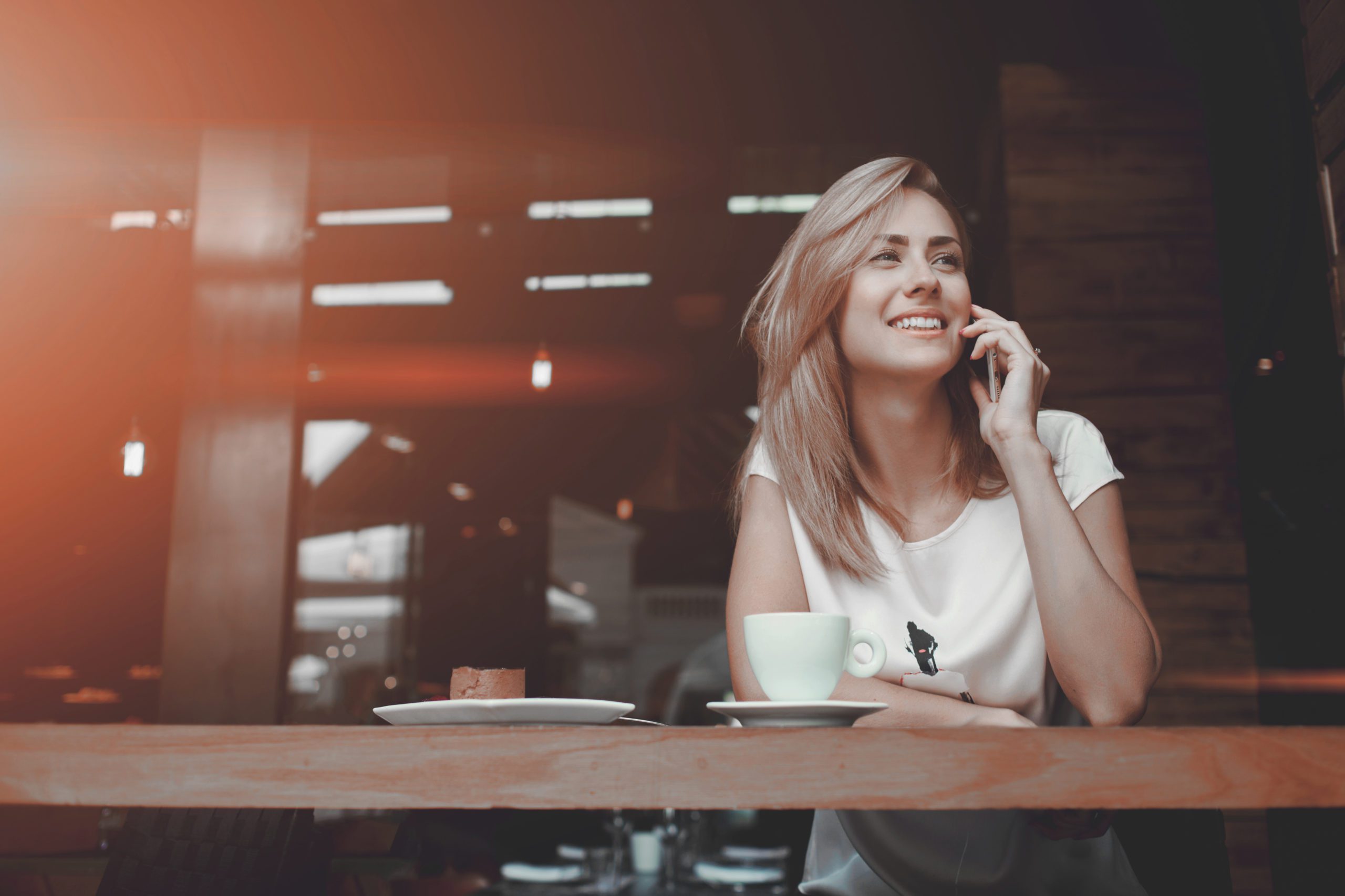 Young charming woman calling with cell telephone while sitting alone in coffee shop during free time, attractive female with cute smile having talking conversation with mobile phone while rest in cafe